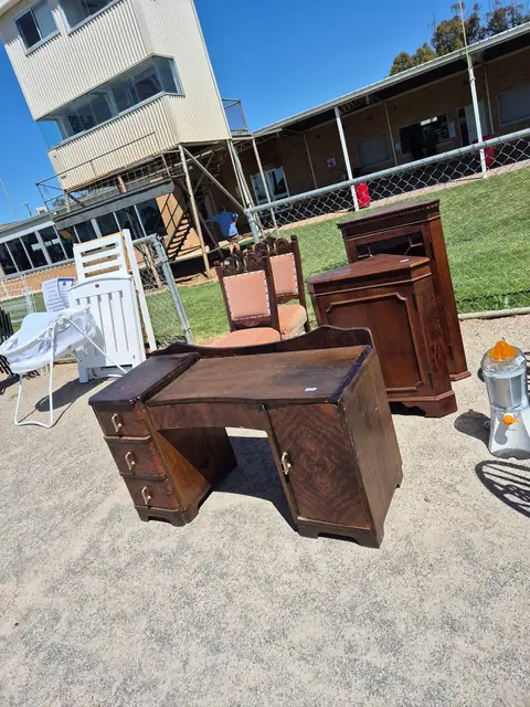 An older timber writing desk, a dressing table, a cabinet and chairs set out on the grass.