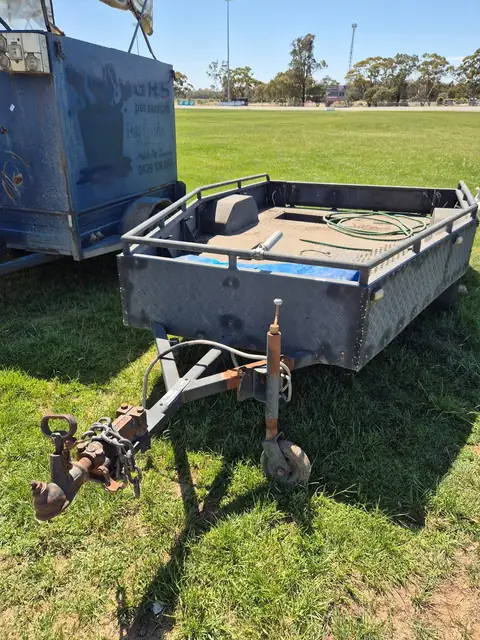 A box trailer with mesh rails, its jockey wheel down and a coil of hose in the tray.
