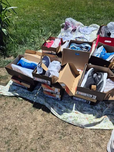 A dozen boxes of shoes and boots laid out on a sheet on the grass.